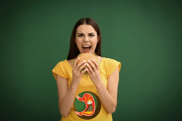 营养不良会导致胃灼热或其他肠胃问题 女人吃绿色背景的汉堡包 胃与喷发火山的说明为酸消化不良 — 图库照片