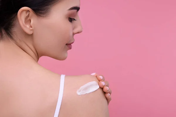 stock image Beautiful woman with smear of body cream on her shoulder against pink background, back view. Space for text