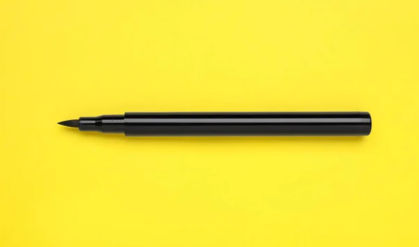Eyeliner marker on yellow background, top view. Makeup product