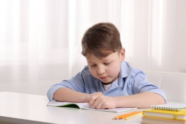 Küçük çocuk içerideki beyaz masadaki defterindeki hatayı siliyor.