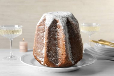 Delicious Pandoro cake decorated with powdered sugar and sparkling wine on white wooden table, closeup. Traditional Italian pastry