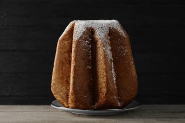 Lezzetli Pandoro keki, siyah arkaplana karşı ahşap masada pudra şekerle süslenmiş. Geleneksel İtalyan pastası