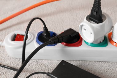Beyaz halıda elektrik prizleri olan uzatma kablosu, yakın plan.