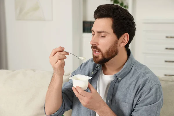 一个英俊的男人在家里的沙发上吃美味的酸奶 — 图库照片