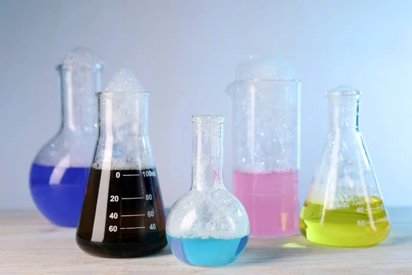 Laboratóriumi Üvegáru Színes Folyadékkal Fehér Asztalon Világoskék Háttérrel Kémiai Reakció — Stock Fotó
