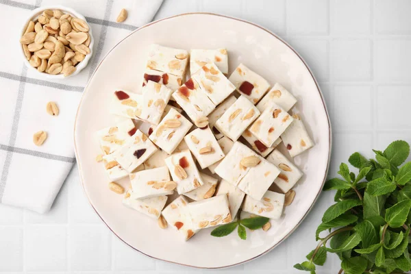 Stock image Pieces of delicious nutty nougat, peanuts and mint on white table, flat lay