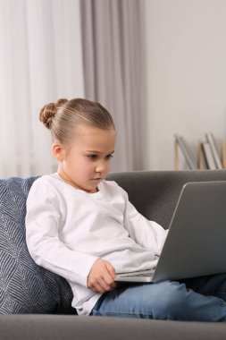 Evdeki kanepede dizüstü bilgisayar kullanan küçük bir kız. İnternet bağımlılığı