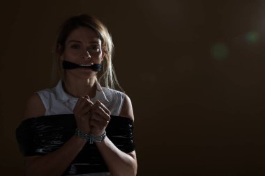 Scared woman taped up and taken hostage on dark background. Space for text