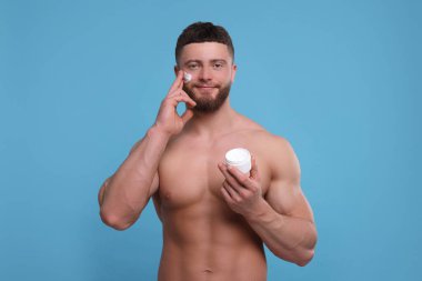 Yakışıklı bir adam açık mavi arka planda yüzüne krem sürüyor.