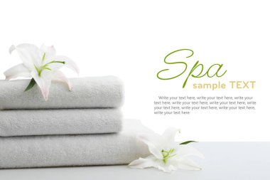 Spa prosedürleri için bir yığın yumuşak havlu ve beyaz arka planda duran zambak çiçekleri. Metin için alanı olan tasarım
