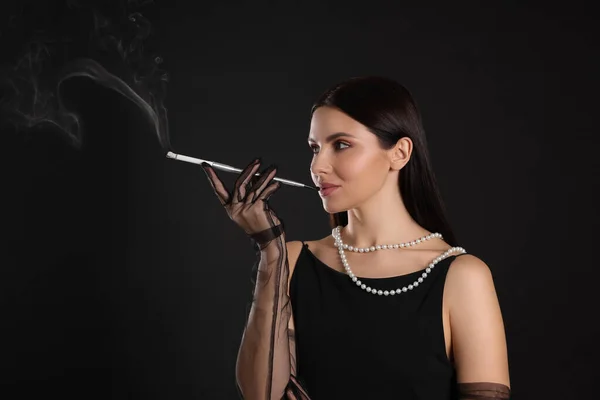 黒い背景でタバコを吸うために長いタバコホルダーを使用する女性 テキストのためのスペース — ストック写真