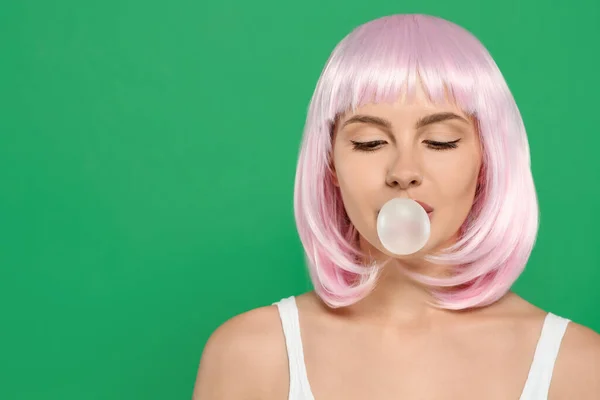Beautiful woman blowing bubble gum on green background, space for text