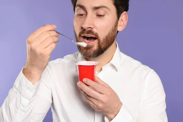 一个英俊的男人在紫罗兰的背景下吃美味的酸奶 — 图库照片