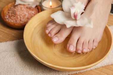 Ayaklarını su ve çiçekle kaseye sokan kadın, yakın plan. Pedikür prosedürü