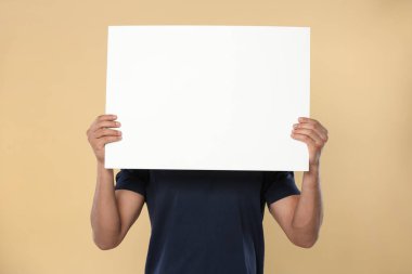 Man holding sheet of paper on beige background, closeup. Mockup for design