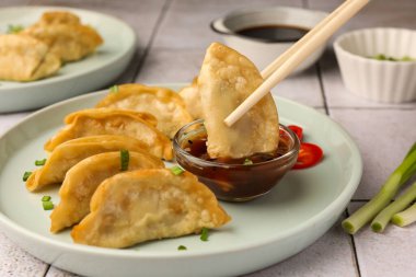 Dipping delicious gyoza (asian dumpling) in bowl with sauce at table, closeup clipart