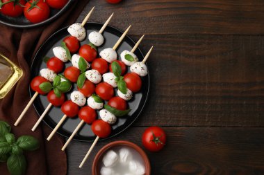 Domatesli şişler, mozzarella topları, fesleğen ve baharatlar ahşap masada, düz yatak. Metin için boşluk