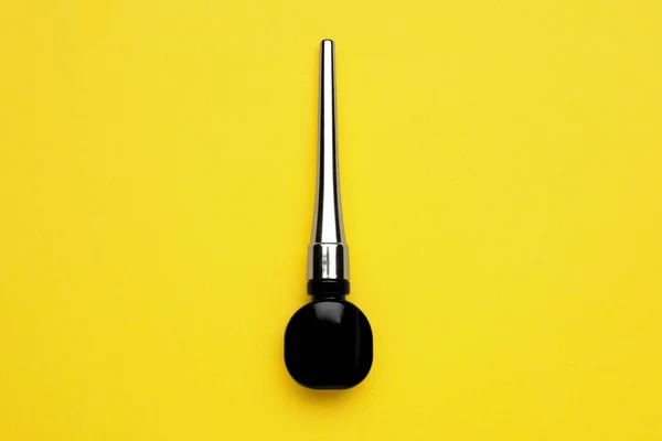 Black eyeliner on yellow background, top view. Makeup product
