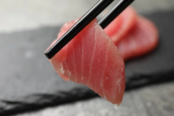 Segurando Saboroso Sashimi Pedaço Atum Cru Fresco Com Pauzinhos Contra — Fotografia de Stock