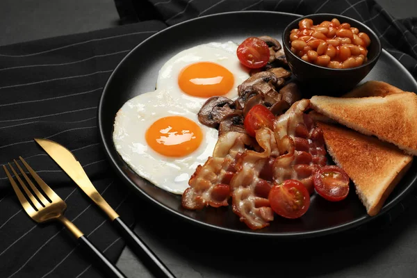 揚げ卵とプレート キノコ ベーコン トマトと黒テーブルの上にトーストパン クローズアップ 伝統的な英語の朝食 — ストック写真