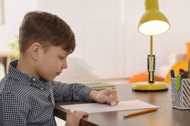 Küçük çocuk içerideki ahşap masadaki defterindeki hatayı siliyor.