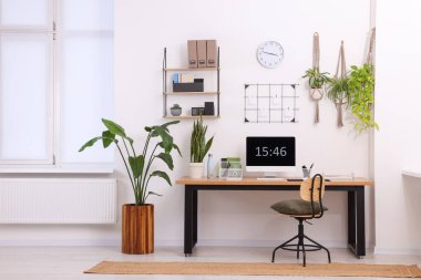 Bilgisayarlı, modern mobilyalı ve evdeki ev bitkileriyle rahat bir iş yeri.