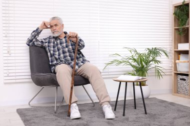 Bastonlu yaşlı adam evinde koltukta oturuyor.