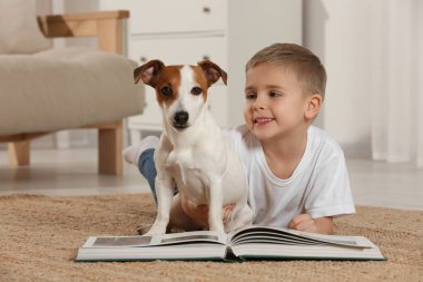 Kitaplı küçük bir çocuk ve sevimli köpeği evde yerde yatıyor. Sevimli hayvan.