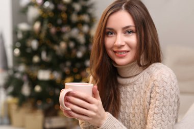 Evinde Noel ağacının yanında bir fincan çayla gülümseyen güzel genç kadın, mesaj için yer.