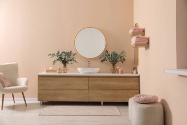 Modern bathroom interior with stylish mirror, eucalyptus branches, vessel sink and wooden vanity
