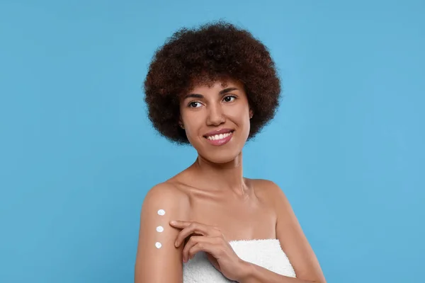 Mooie Jonge Vrouw Aanbrengen Lichaam Crème Arm Licht Blauwe Achtergrond — Stockfoto