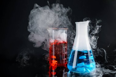 Laboratory glassware with colorful liquids and steam on black background. Chemical reaction