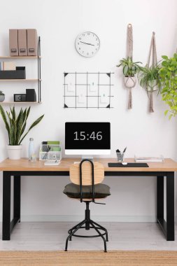 Bilgisayarlı, modern mobilyalı ve evdeki ev bitkileriyle rahat bir iş yeri.