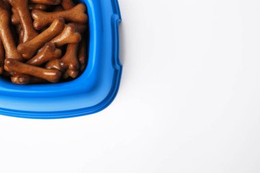 Beyaz arka planda kemik şekilli köpek kurabiyeleri olan mavi kase, üst manzara. Metin için boşluk