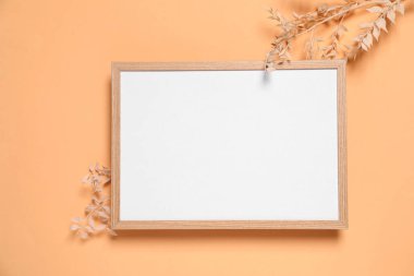 Boş fotoğraf çerçevesi ve soluk turuncu arka planda kuru dekoratif bitkiler. Tasarım için boşluk