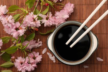 Bir kase soya sosu, yemek çubukları ve bambu hasırında çiçek açan güzel bir dal.