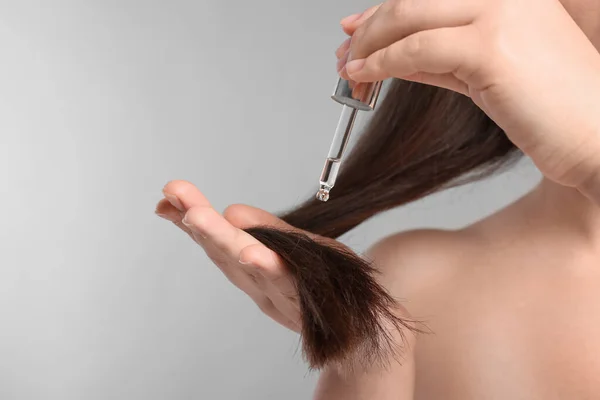 ライトグレーの背景に髪にエッセンシャルオイルを適用する女性 クローズアップ — ストック写真