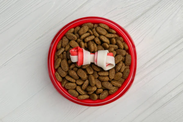 stock image Dry dog food and treat (knotted chew bone) on white wooden floor, top view