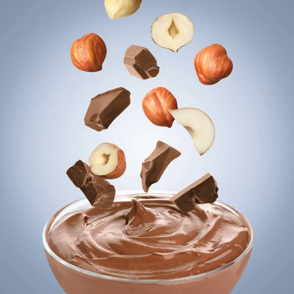 Making yummy chocolate paste. Hazelnuts and pieces of chocolate falling into bowl on light blue background