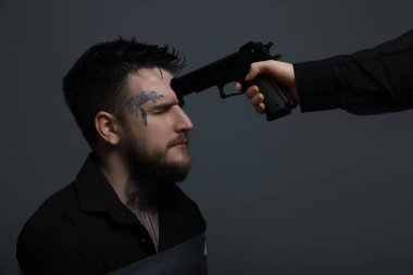 Kaçıran kişi gri arka planda rehin alınan bantlanmış bir adama silah doğrultuyor.