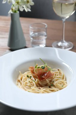 Prosciutto ve mikroyeşillikli lezzetli spagetti ahşap masada servis edilir, yakın plan. Makarna yemeğinin enfes sunumu