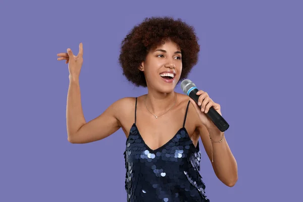 stock image Curly young woman with microphone singing on purple background