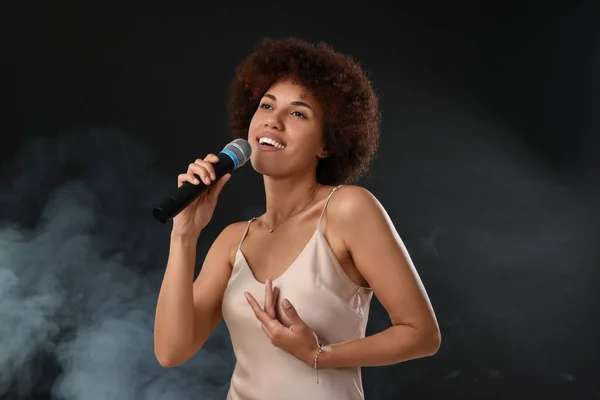 stock image Curly young woman with microphone singing in smoke on black background