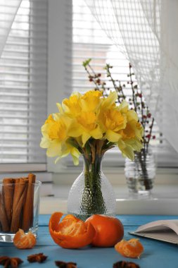 Vazoda güzel sarı nergisler, açık mavi masada mandalinalar ve tarçın.