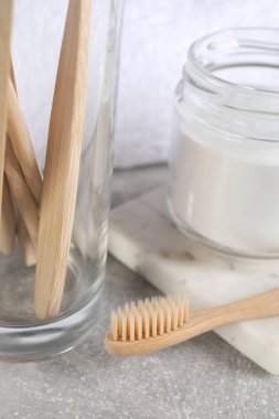 Bambu diş fırçaları ve açık gri masada bir kavanoz kabartma tozu, yakın plan.