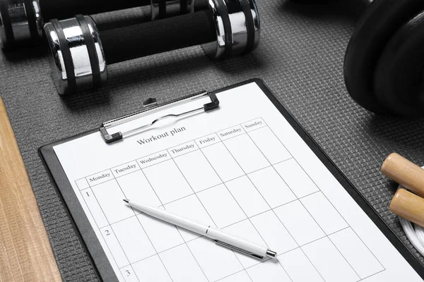 Clipboard with workout plan and sports equipment on wooden table, closeup. Personal training