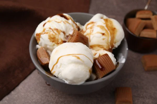 Scoops of ice cream with caramel sauce and candies on textured table, closeup