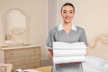 Genç oda hizmetçisi otel odasında bir yığın temiz havlu tutuyor. Metin için boşluk