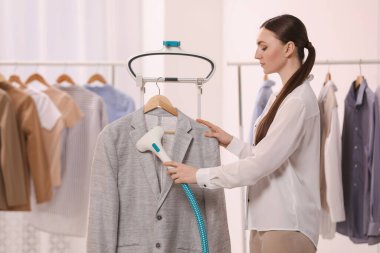 Woman steaming jacket on hanger in room