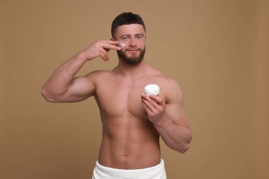 Yakışıklı bir adam soluk kahverengi arka planda yüzüne krem sürüyor.